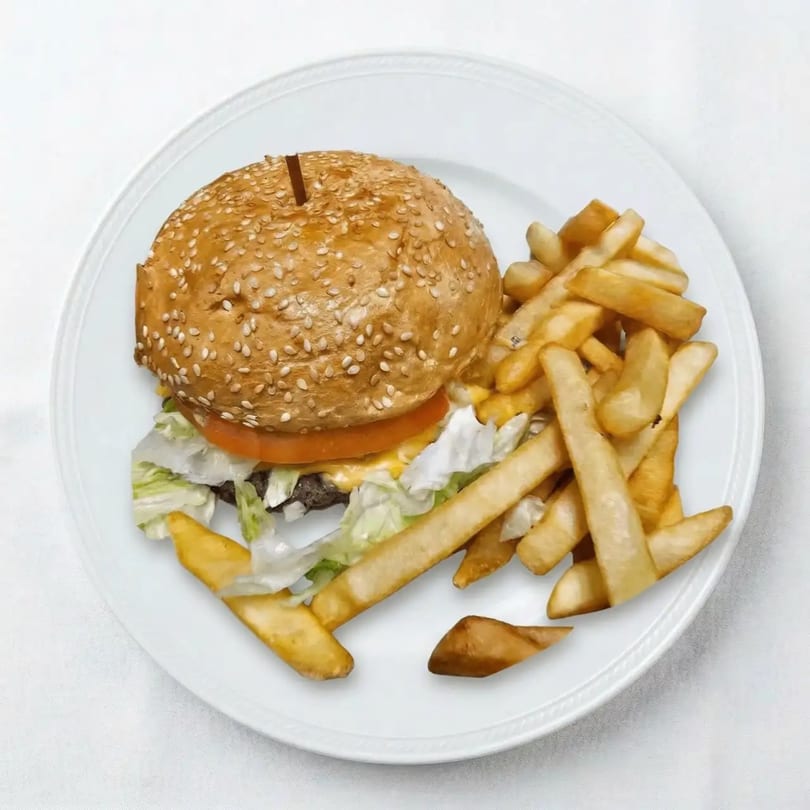 Cheeseburger with lettuce, tomato, and a side of golden french fries on a white plate.